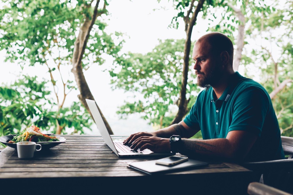 A white male freelancer sitting outside and typing on his laptop